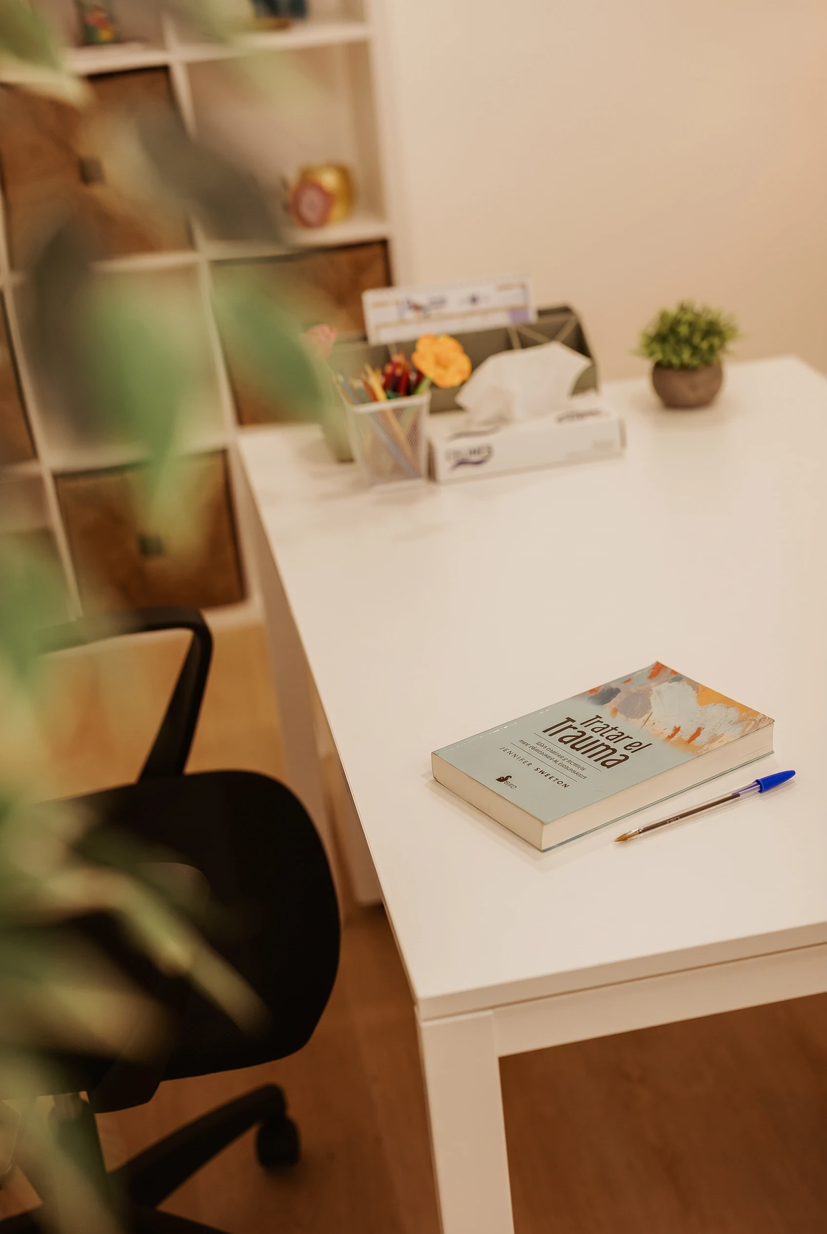 Mesa de la consulta con un libro sobre el tratamiento del trauma, un bolígrafo y una caja de pañuelos.