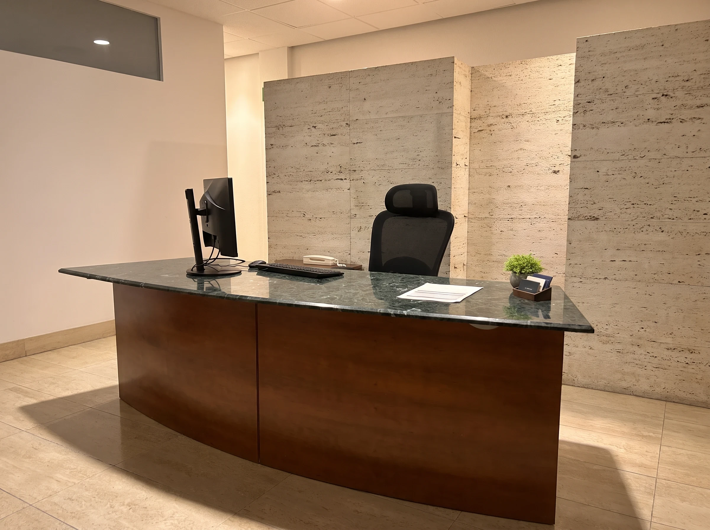 Mostrador de recepción del centro Psiconervión Bilbao – Abando, de madera con encimera de mármol verde, ante una pared de travertino.