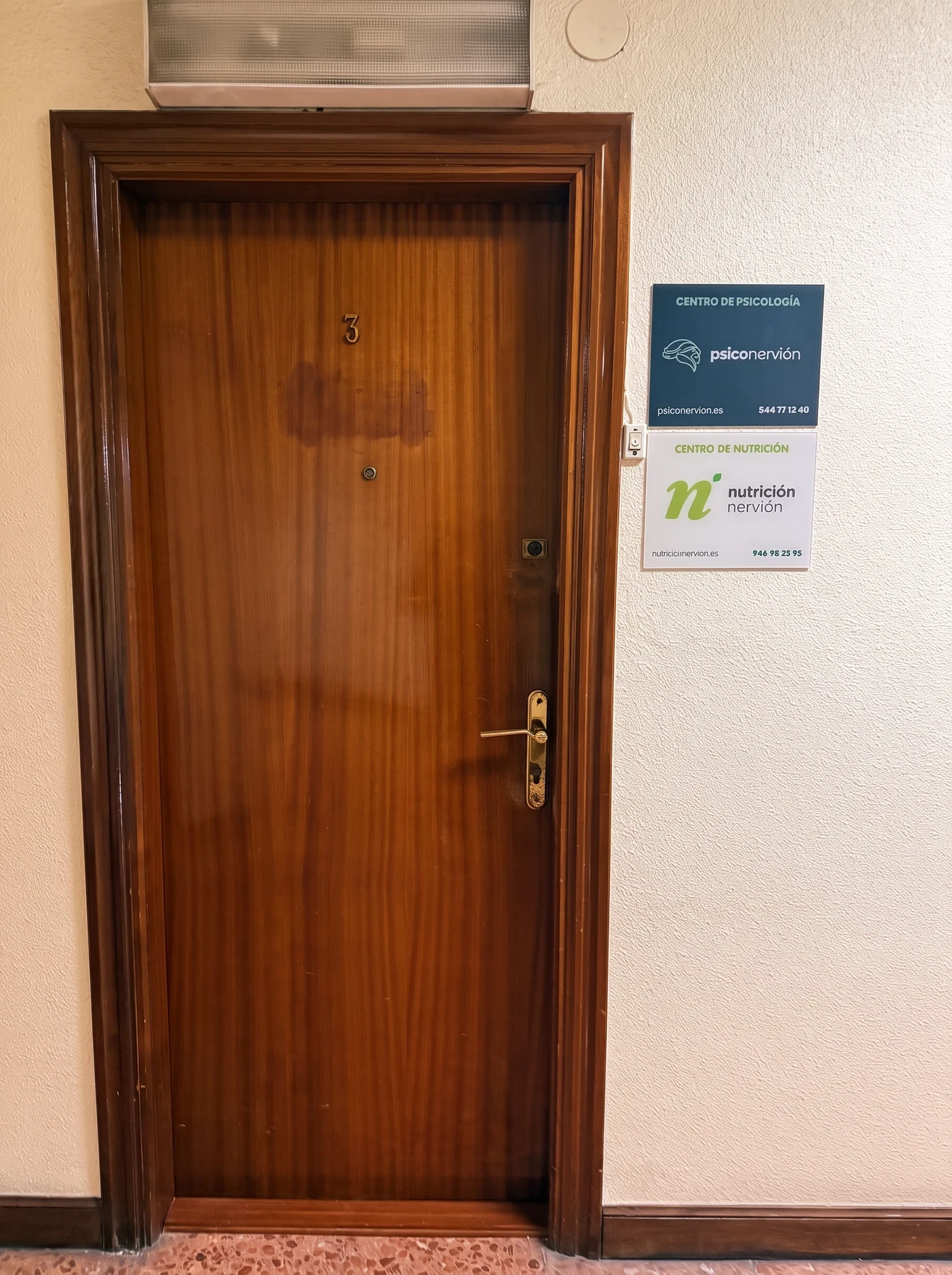 Puerta de madera del piso con las placas de Psiconervión y Nutrición Nervión en la pared.