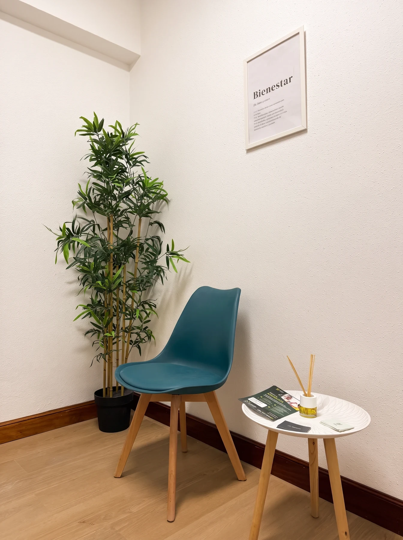 Sala de espera con una silla turquesa, una mesita con un difusor, un bambú y un cuadro con la palabra «Bienestar».