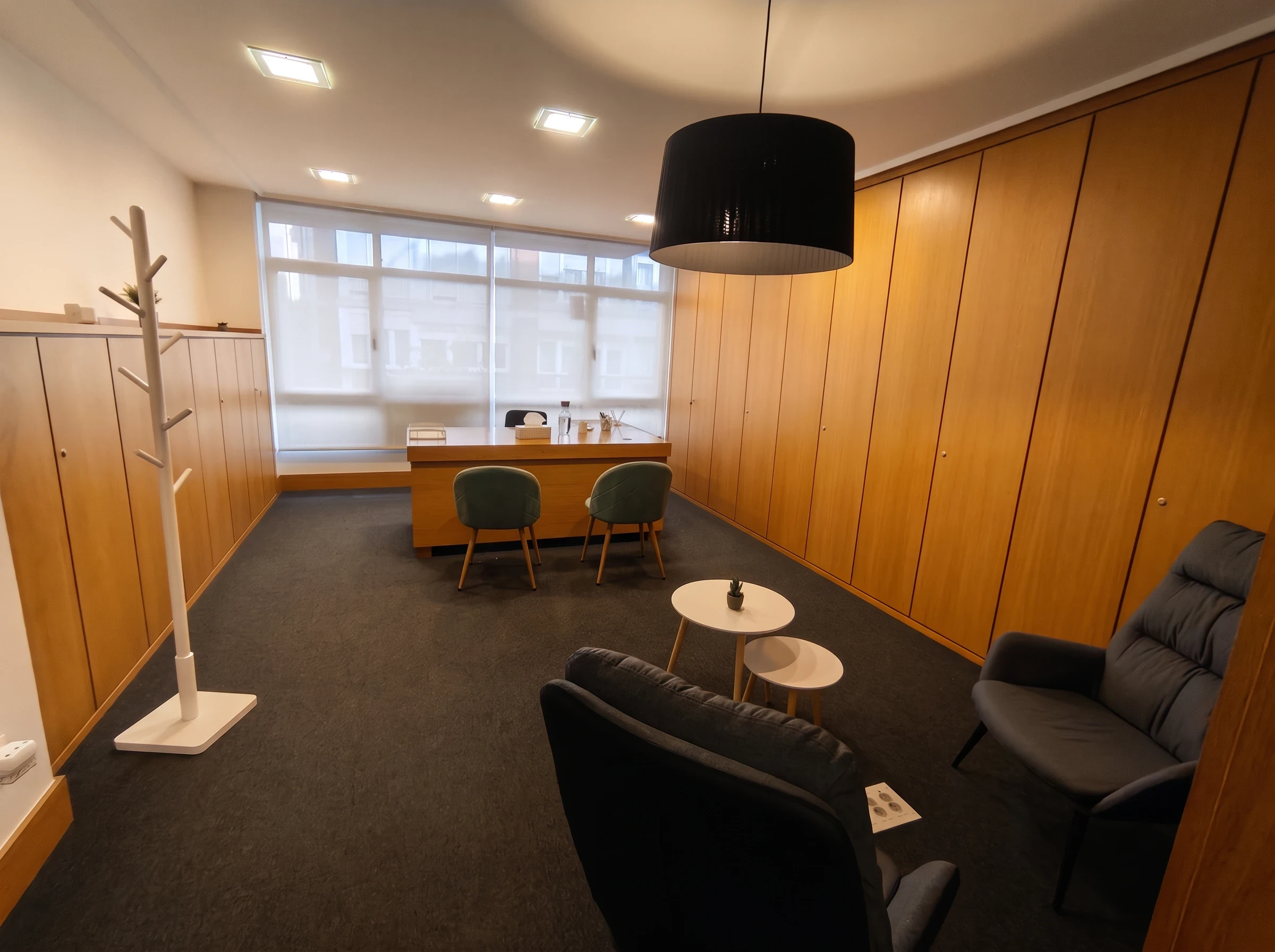 Consulta amplia del centro Psiconervión Getxo – Las Arenas, con paredes de madera, lámpara colgante negra, dos butacas y el escritorio junto a las ventanas.