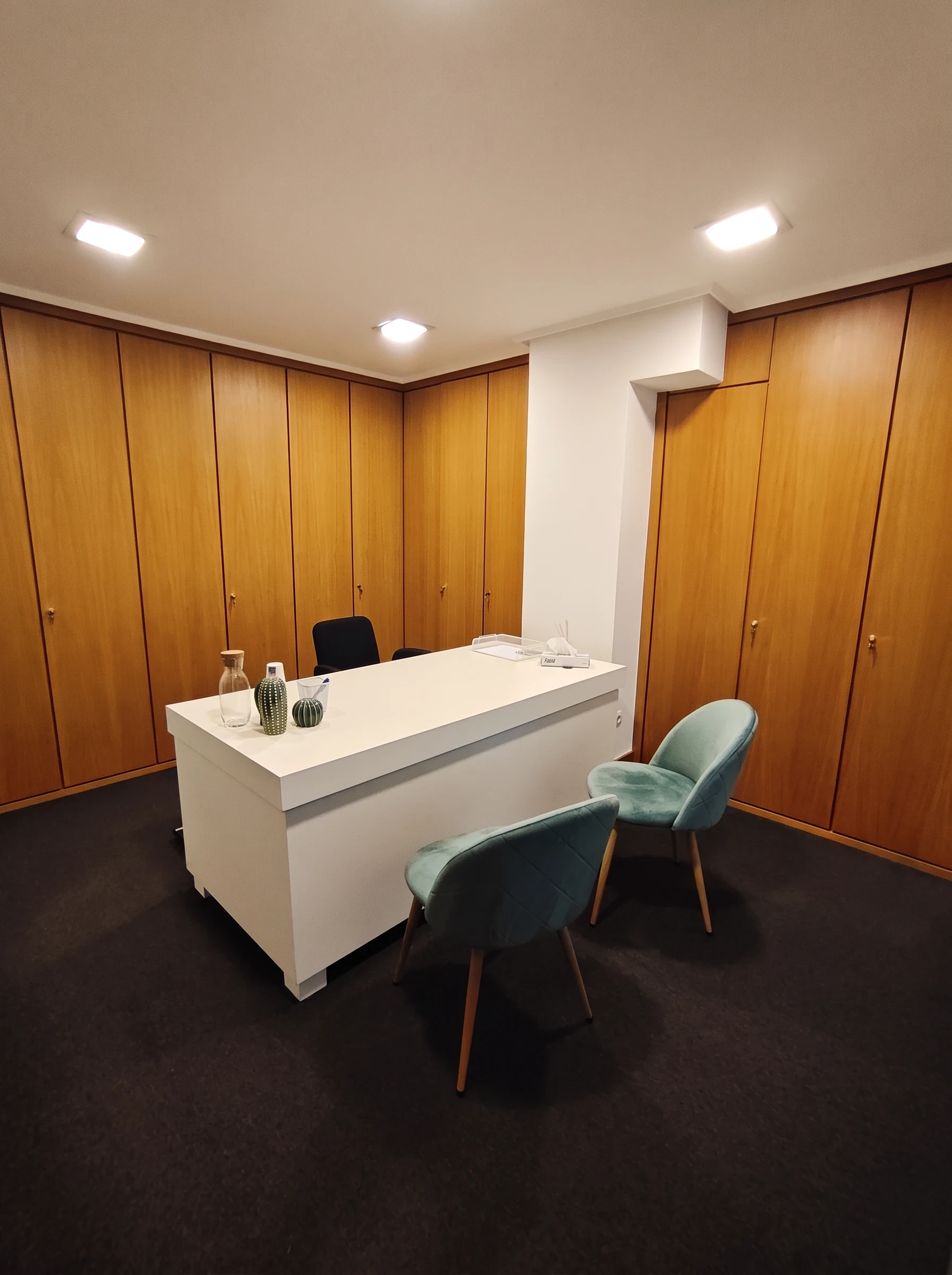 Consulta con paredes de madera, mesa blanca y dos sillas verde azulado.
