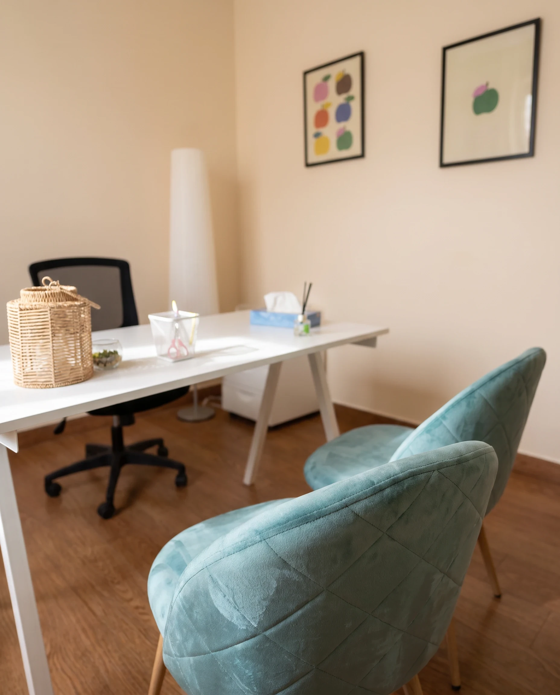 Consulta con escritorio blanco, silla de trabajo y dos butacas turquesa para el paciente.
