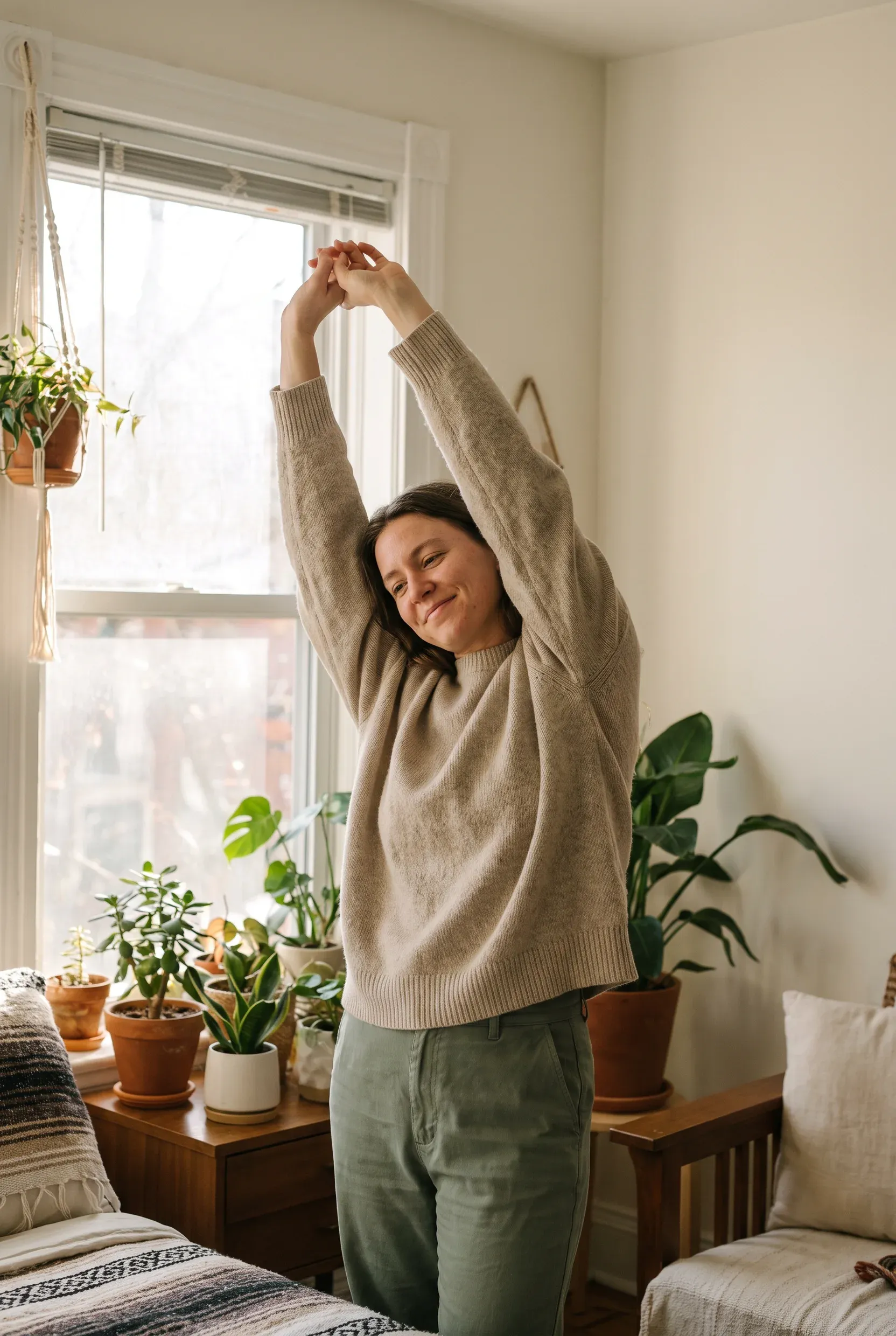 Una persona estira los brazos junto a una ventana luminosa con plantas.