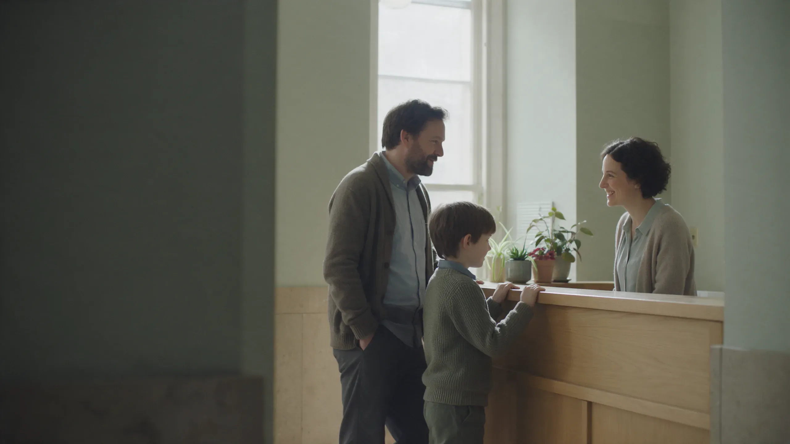 Un padre y su hijo conversan con una profesional en el mostrador de recepción de un centro de psicología.