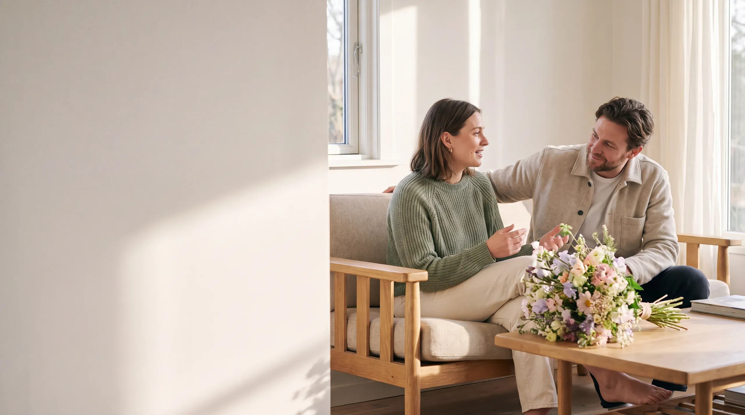 Dos personas conversan con calidez en una habitación luminosa con flores de colores.